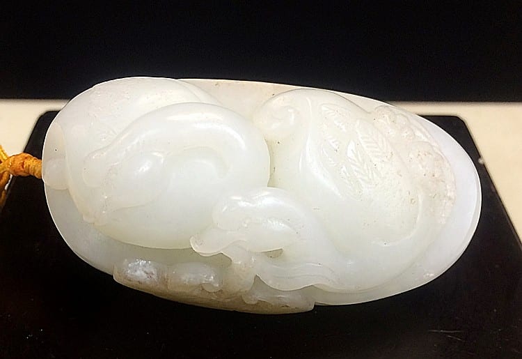 Close-up of a white jade pendant or carved ornament shaped with a rounded, animal-like relief on a black display mount.