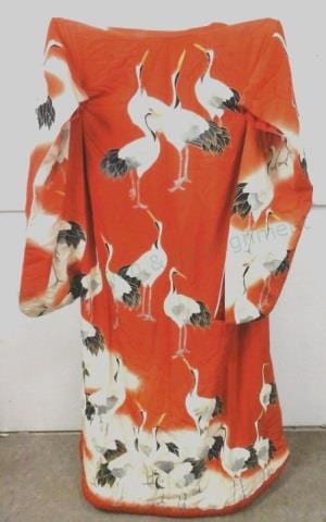 Orange kimono robe fabric with repeating white bird and floral motifs, shown folded and draped against a light background.