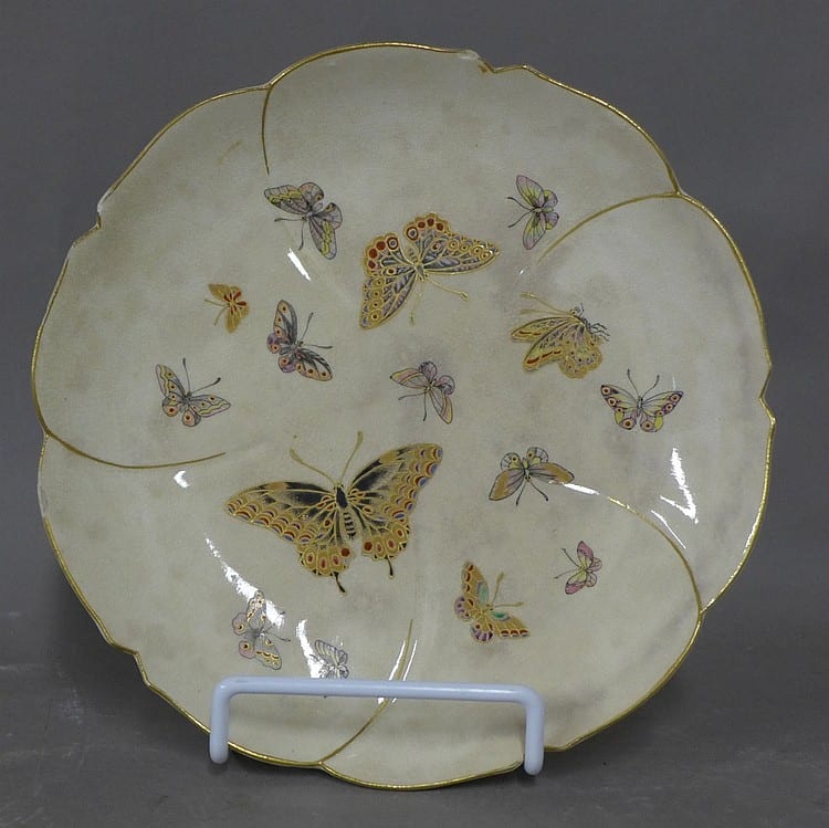 Round ceramic plate with gold rim and colorful butterfly and floral designs on a white background.
