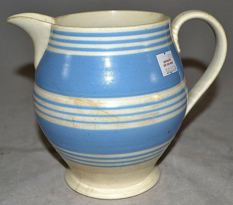 Ceramic pitcher with a curved spout and handle, glazed in white with blue horizontal stripe bands around the body.