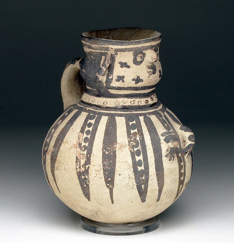 Ceramic figural vessel with a wide round body and short neck, painted in black and cream stripes and symbols, shown against a dark background.