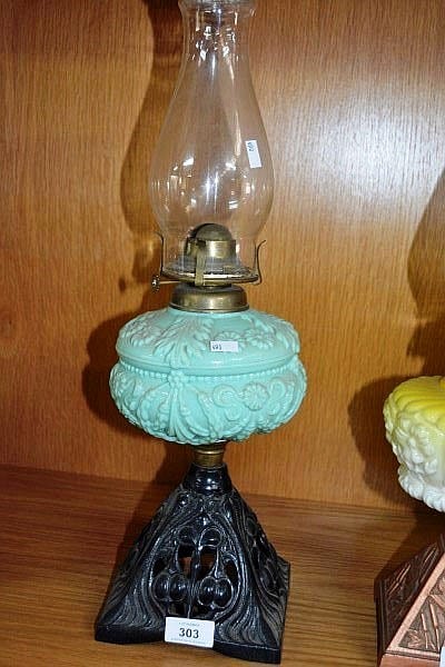 Antique-style oil lamp with a clear glass reservoir and ornate turquoise base on a shelf.