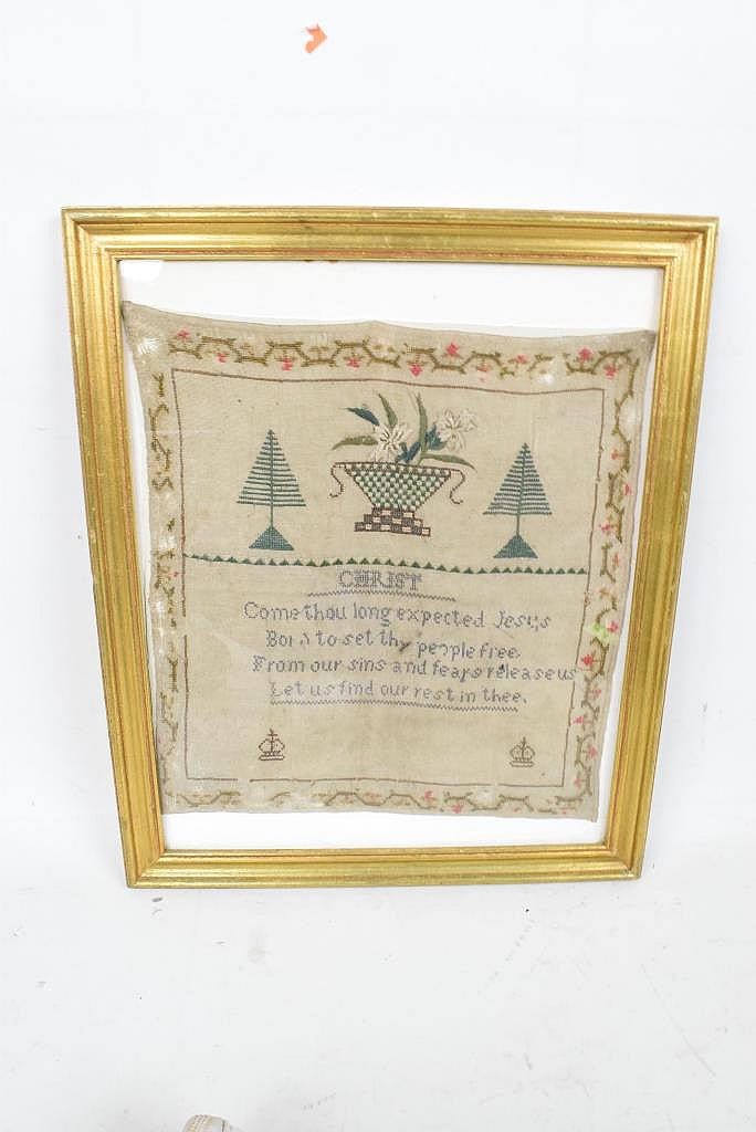 Framed needlepoint sampler featuring trees, a checkered urn or basket, and small decorative borders with stitched text.