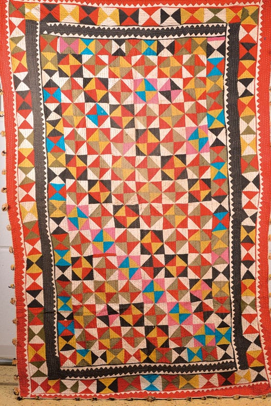 Colorful patchwork quilt with small geometric triangle pieces and a red border, photographed straight-on.