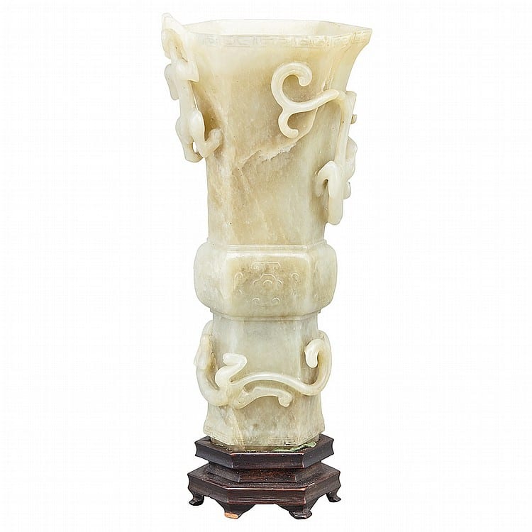 Carved pale jade-like vase with a flared mouth, looping cutout motifs, and a banded body mounted on a dark wooden stand.
