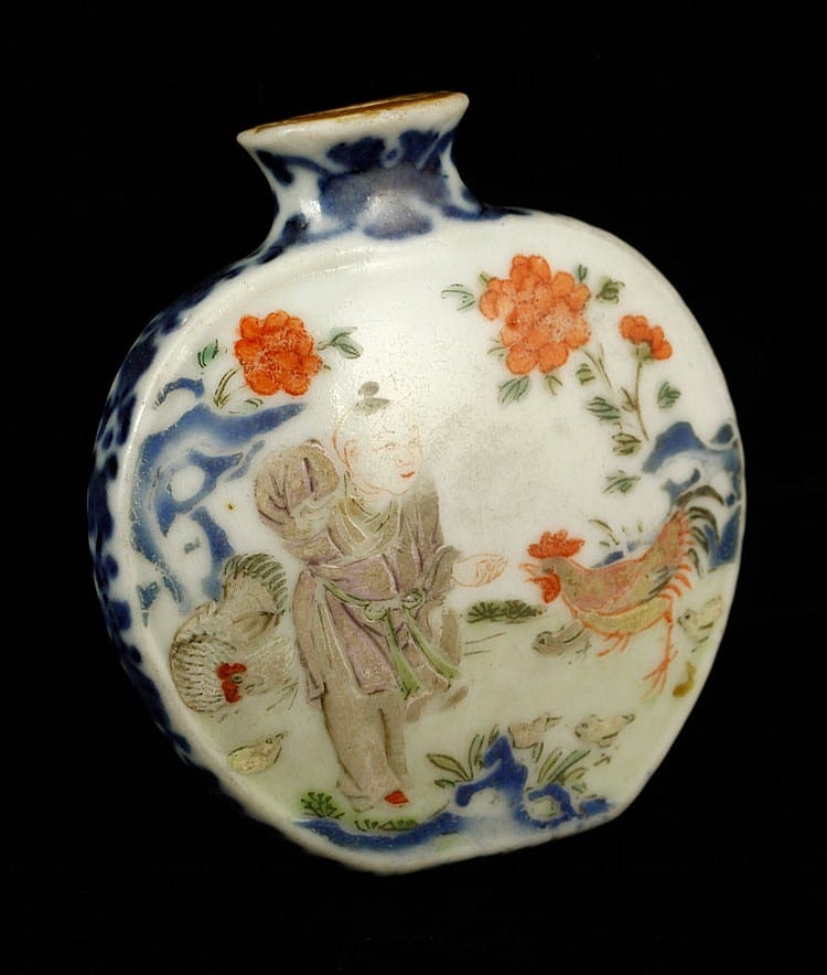 Small white porcelain snuff bottle with blue and orange floral decoration and a figure in the center, shown against a dark background.
