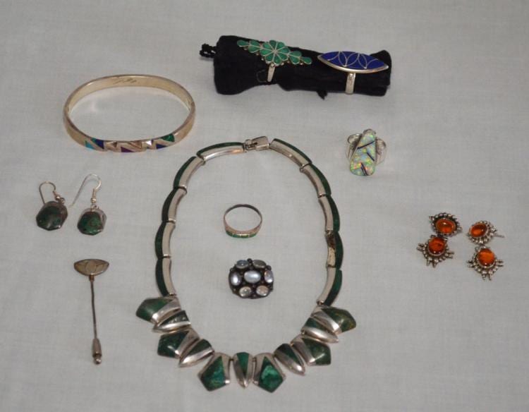 Group of silver-tone jewelry pieces with green and orange stones, including a ring, necklace, earrings, and a bracelet, arranged on a gray background.