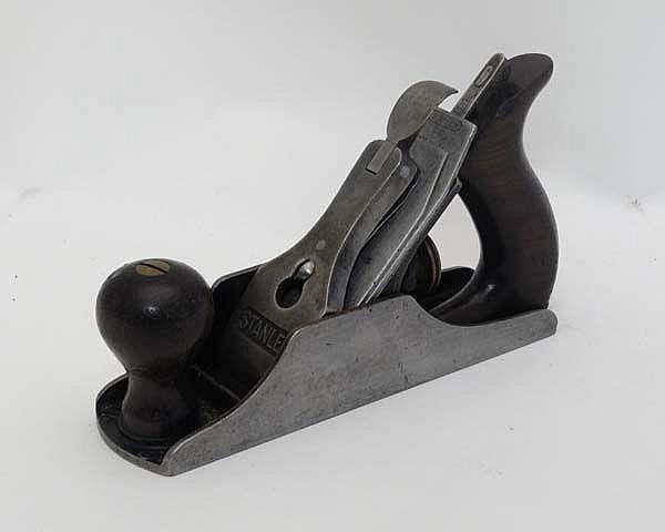 Black and gray vintage metal hand plane tool with wooden knobs and curved handle on a light background.