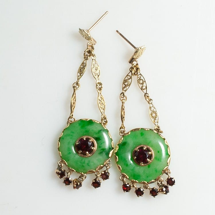 Pair of gold-tone dangling earrings with green oval jade-like drops and red gem centers, linked chains and small red bead accents.