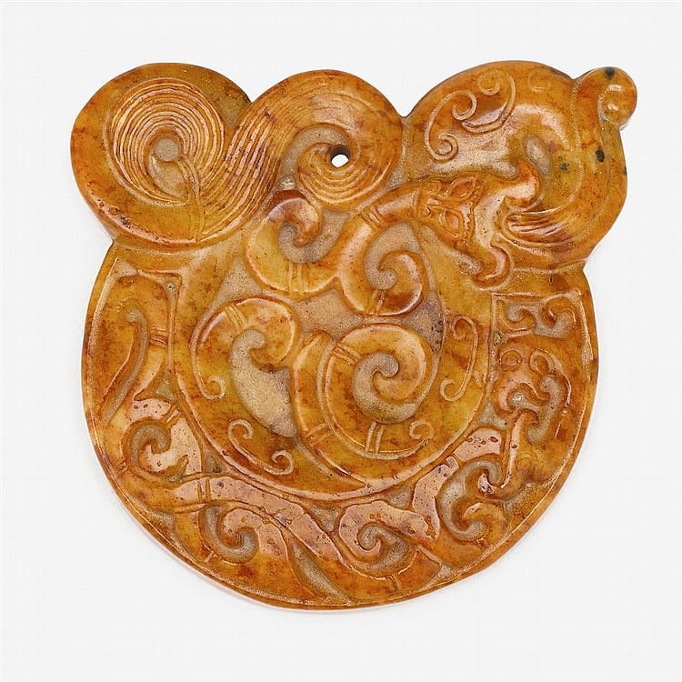 Carved yellow-brown pendant with swirling scrollwork and a stylized animal face, photographed against a white background.