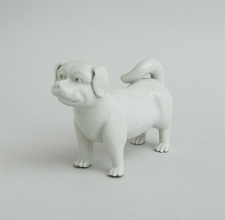 White ceramic dog figurine with a low, forward-leaning stance and detailed face, ears, and paws against a plain light background.