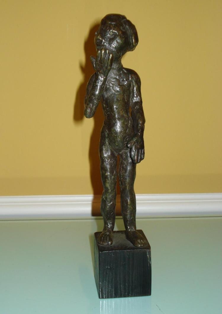 Bronze sculpture of a standing child figure with one hand touching the face, mounted on a rectangular dark base.