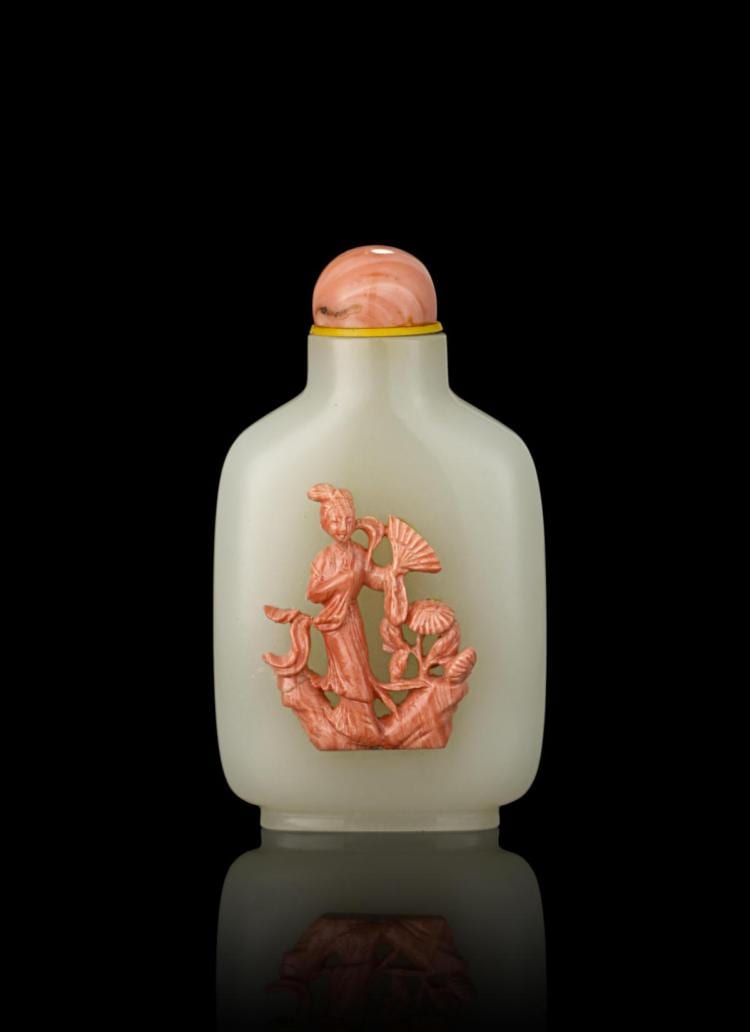 White Chinese snuff bottle with a rounded cap and an orange carved figure holding flowers, shown against a black background.