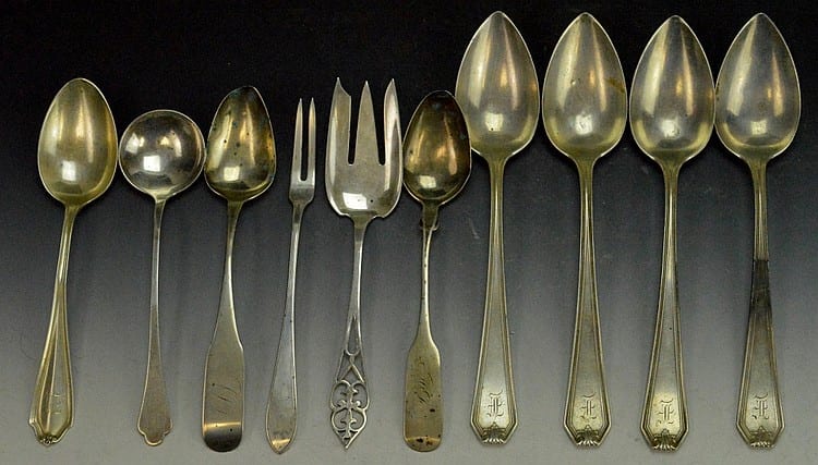 Group of silver-colored flatware utensils on a dark background, including spoons and forks with decorative handles.