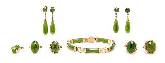 Set of green jade jewelry pieces with gold settings, including drop earrings, a bangle bracelet, and ring and pendant-like pieces laid out together.