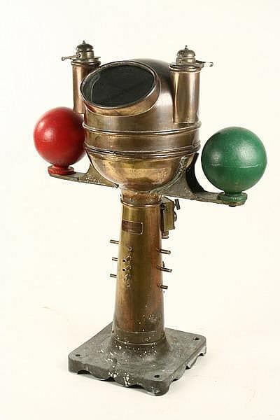 Brass ship’s binnacle with a compass housing and two colored signal balls, photographed on a gray base.