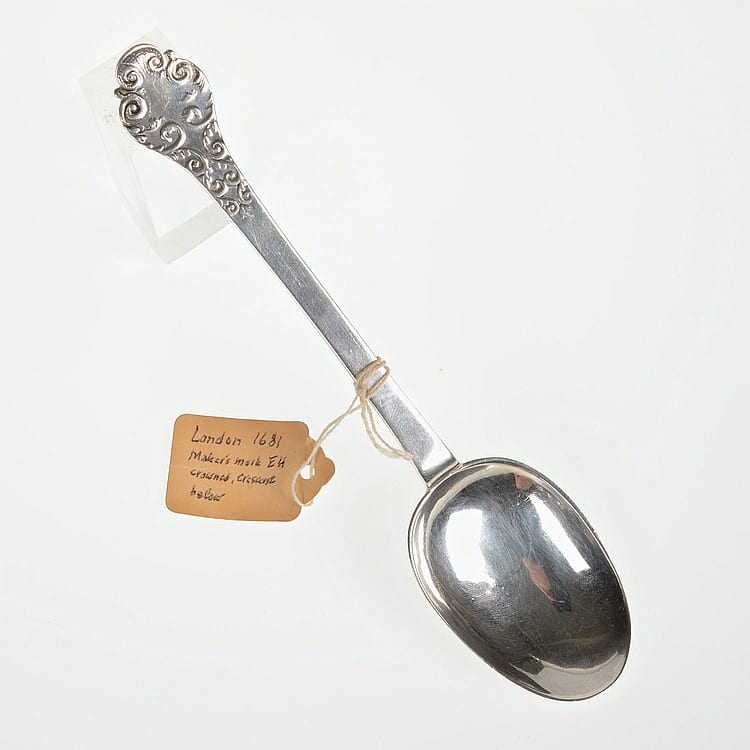 Close-up of a silver-toned decorative serving spoon with an ornate oval bowl and engraved handle details, photographed on a white background.