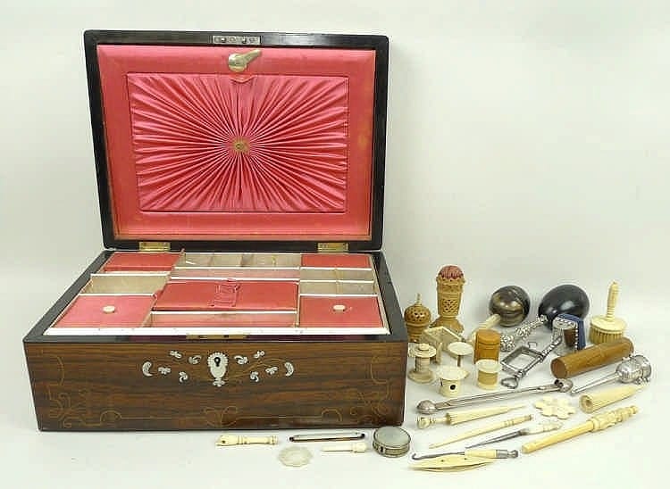 Open wooden sewing box with compartments and decorative red lid panel, next to sewing notions like scissors, needles, and spools.