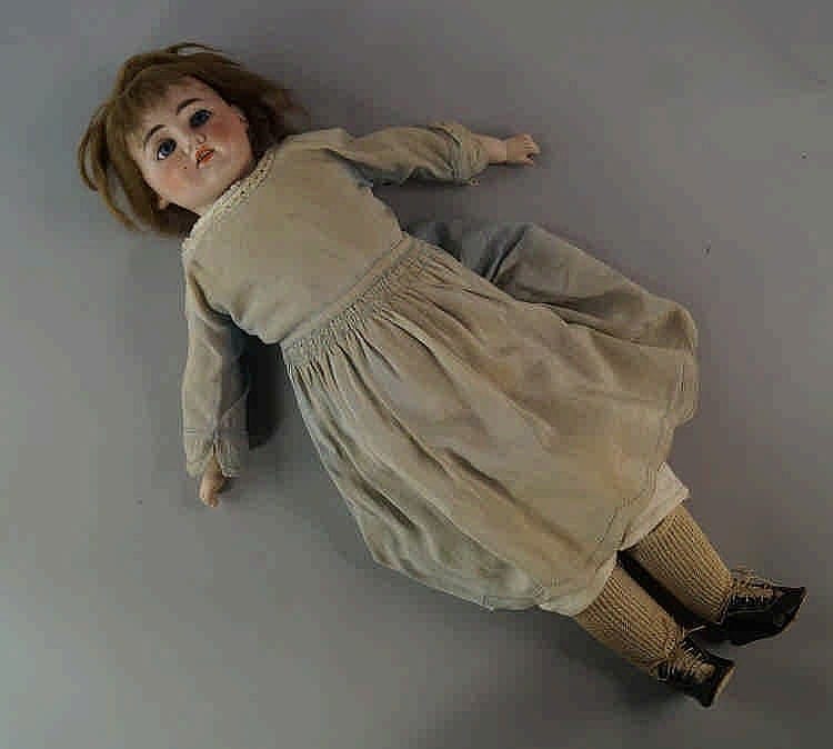 A doll with a painted porcelain-like face, brown wig, and a cream dress with gathered skirt, lying on its side with one arm extended.