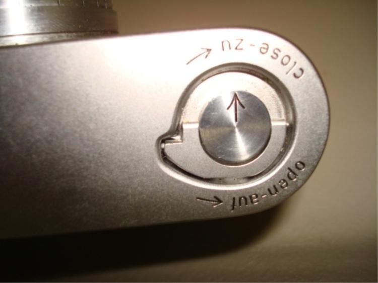 Close-up of a silver camera dial with a circular center and arrow markings around the rim.