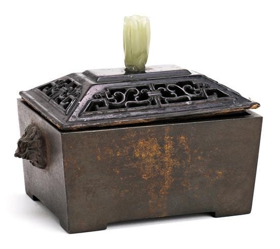Bronze incense burner with rectangular body, carved lid details, and a small pale-green smoke plume rising from the top.