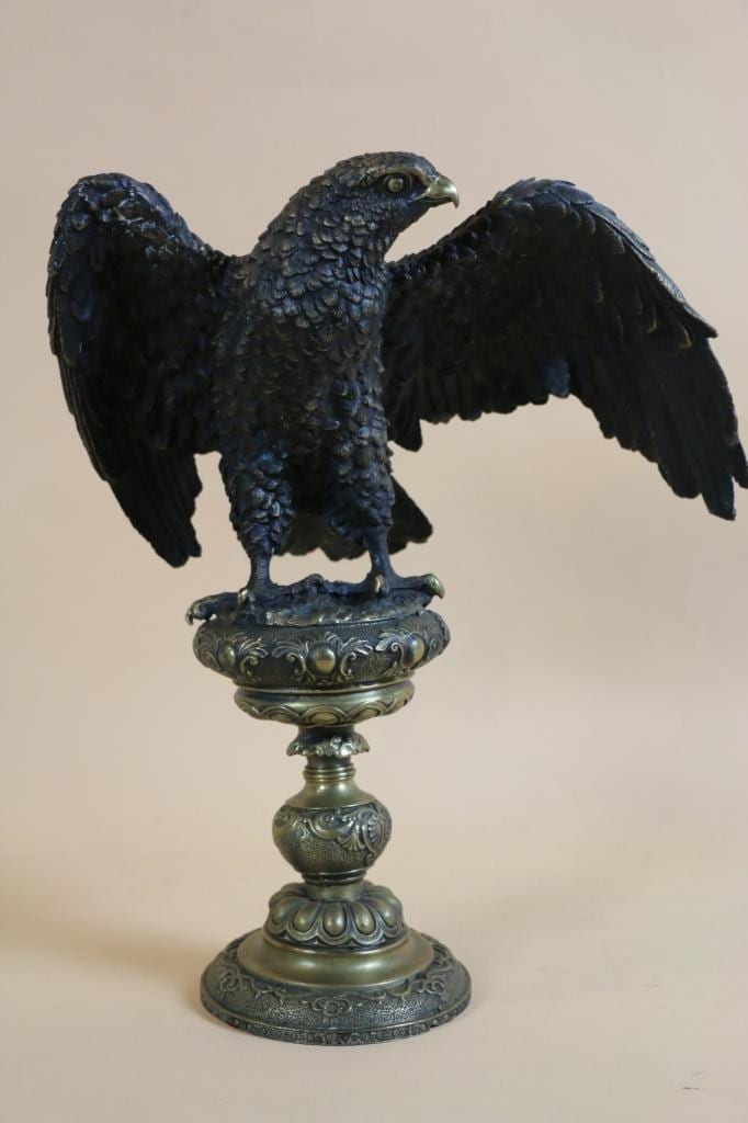 Bronze-colored eagle sculpture with wings spread, perched on an ornate pedestal base.