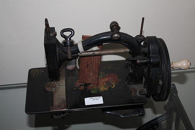 Small antique-style sewing machine with a hand crank, black metal base, and wood accents, photographed against a light background.