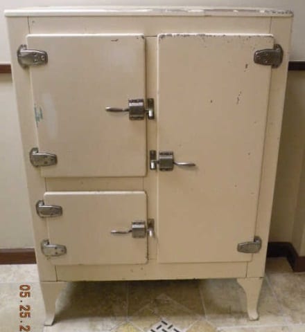 Front view of a cream-colored antique ice box refrigerator with two doors and metal latches and handles.