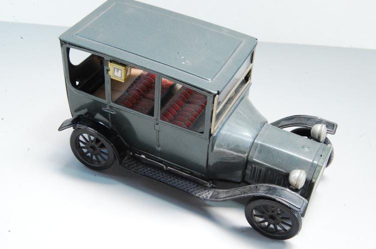 Vintage gray tin toy car with red interior seats, shown three-quarter view on a white background.