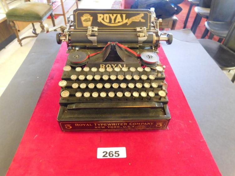 Black vintage typewriter with “ROYAL” on the front, shown on a red cloth table covering.