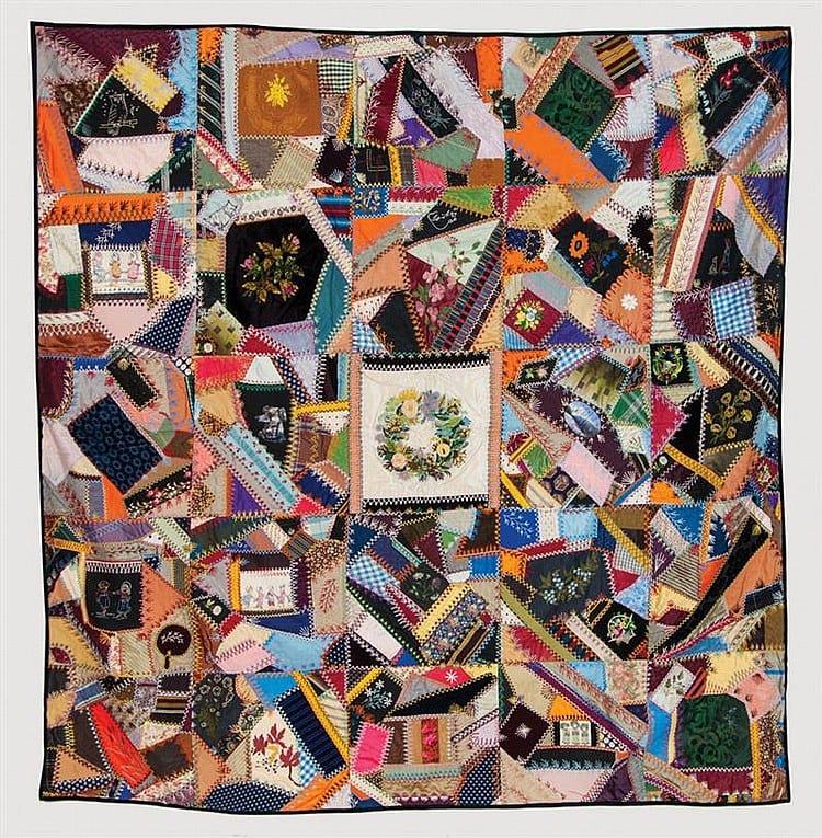Close-up of a Victorian-style crazy quilt with colorful patchwork squares and small embroidered fabric designs in orange, blue, green, and purple.