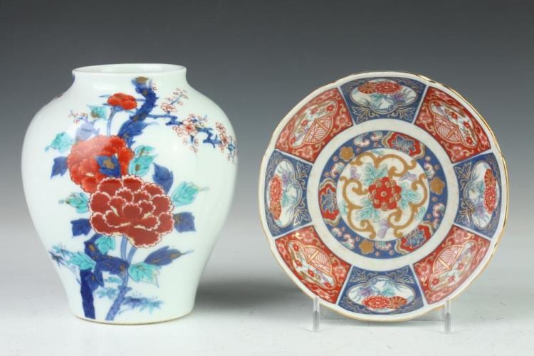 Two Japanese porcelain pieces on a stand: a white vase with blue and red flowers, and a decorative plate with a multicolor floral center and ornate border.