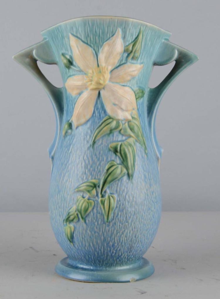 Blue ceramic vase with scalloped rim, two side handles, and raised floral decoration with cream flower and green leaves.