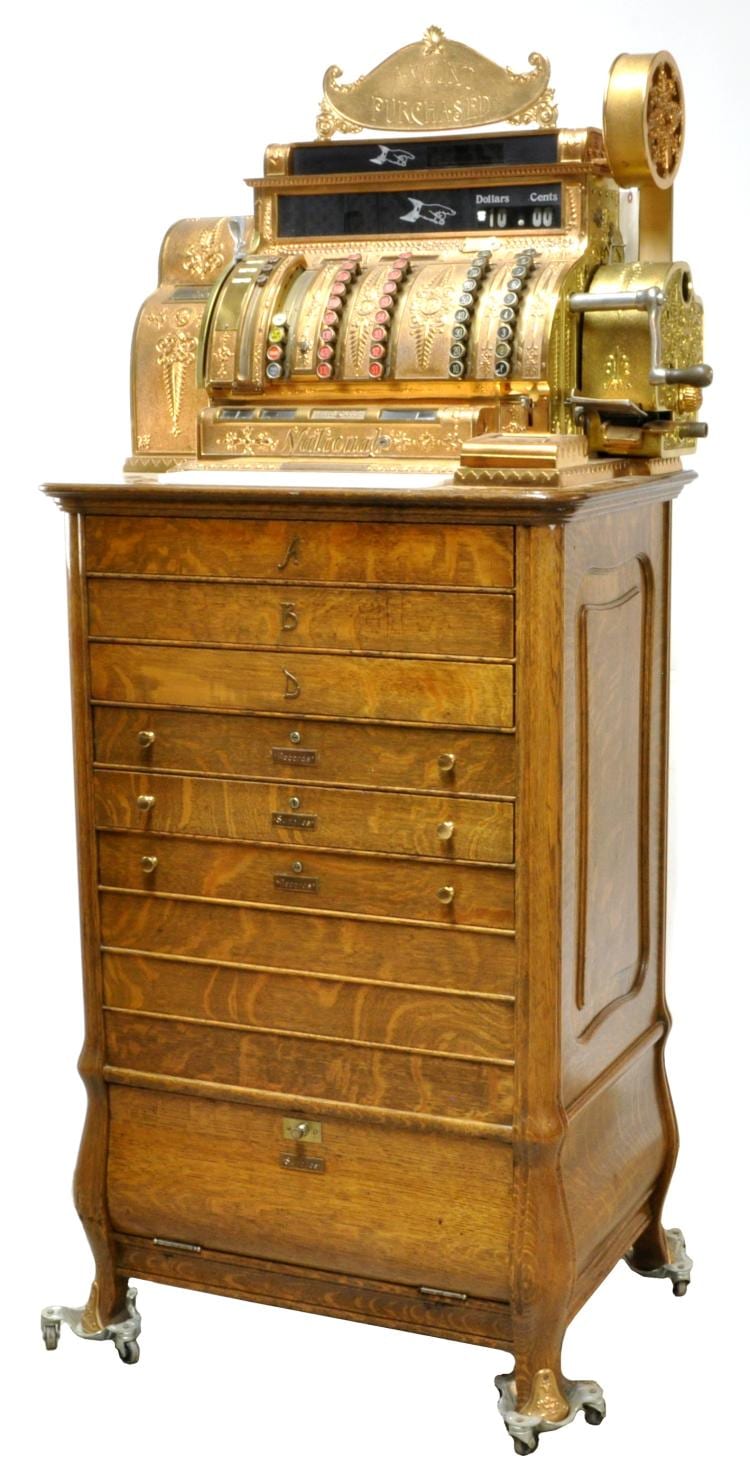 Brass antique cash register with numbered dials, coin mechanism, and a front drawer on four carved feet.