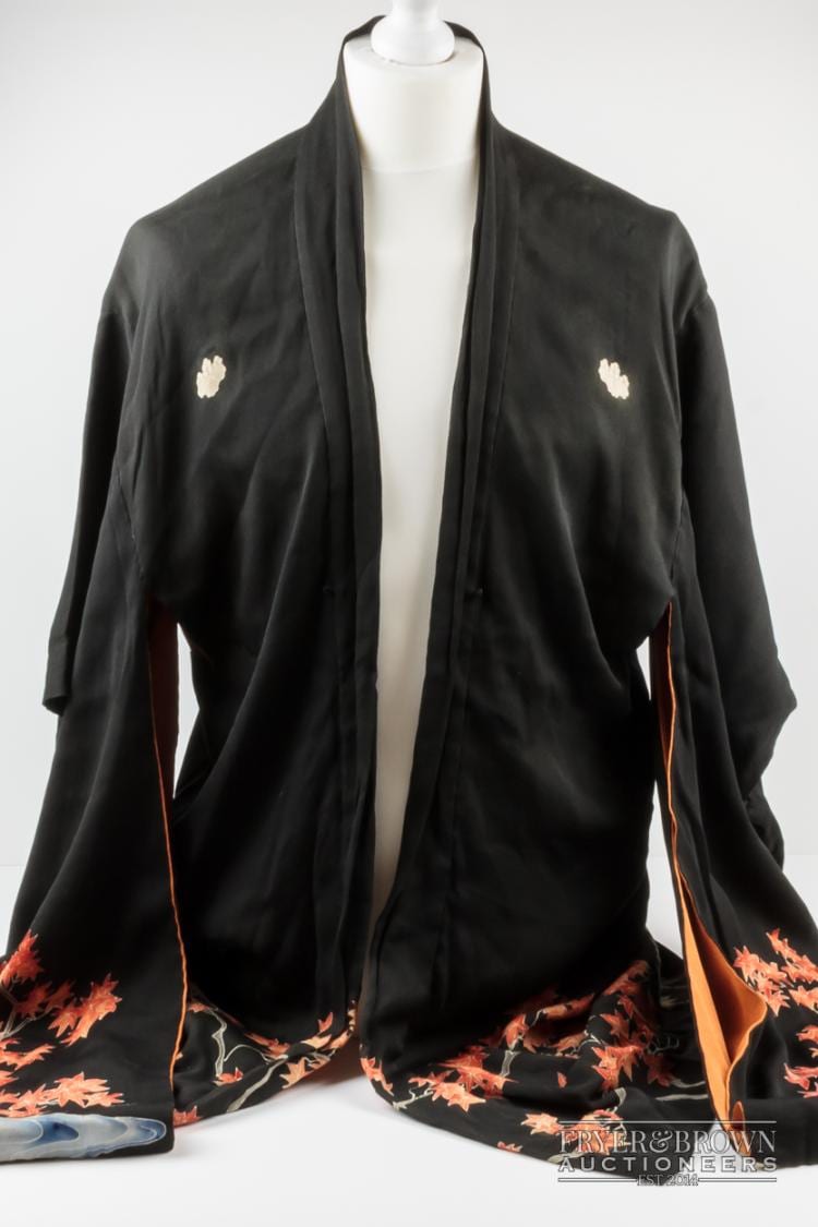 A vintage women's Japanese silk crepe haori/short kimono, the black crepe silk with pattern of red and green acer trees with bridge and river below the waistline, the lining of burnt orange with fuller design of cherry blossoms, the upper shoulders applied with kiri-mon or paulownia crests, 99cm long approx., the sleeves of ko-furisode length, 78cm approx. sold by Fryer and Brown, lot 503 — auction record photograph