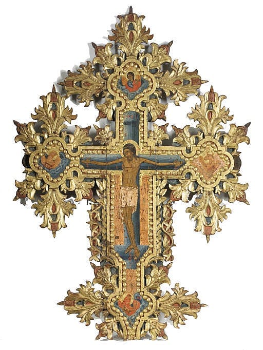 Ornate gilt and painted metal icon with a central crucifix and decorative floral scrollwork around it.