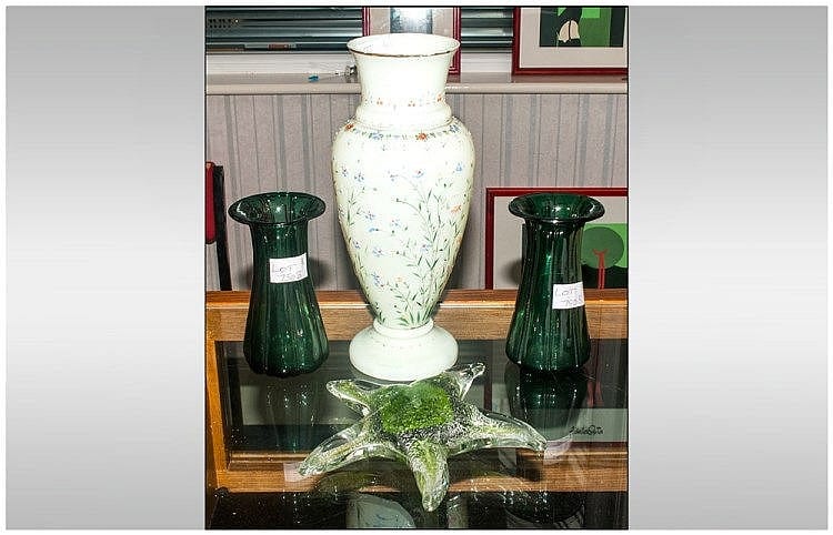 Two green glass vases on a wooden table, with a tall white vase in the center.