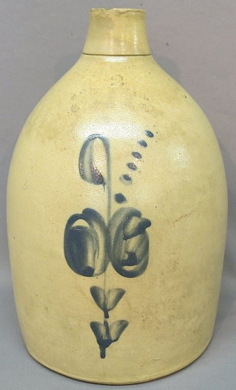 Yellow ceramic stoneware jug with a blue floral and leaf motif on the front and a short neck and wide belly.