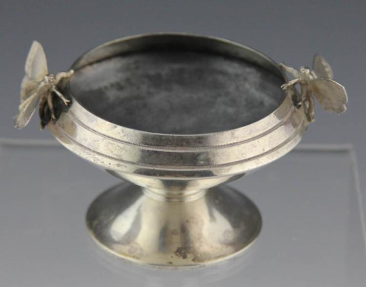 Sterling silver salt cellar with an oval bowl and raised moth-like figures on the rim, shown against a gray background.