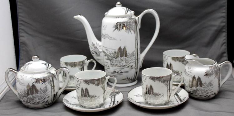 Japanese-style porcelain tea set with teapot and several cups on saucers, decorated with black pine trees and gold accents.