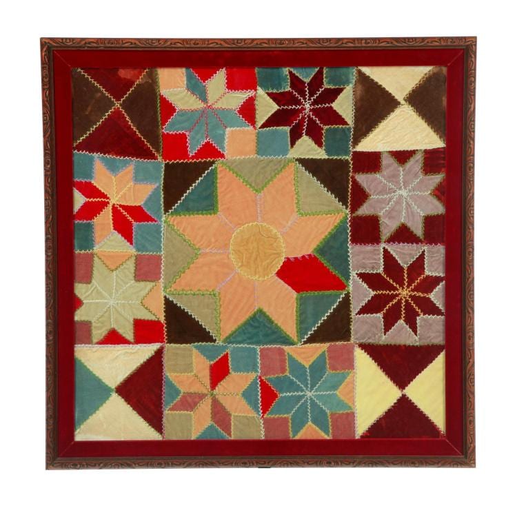Framed patchwork textile quilt with a central orange rosette star surrounded by multicolored geometric blocks and diamond shapes.
