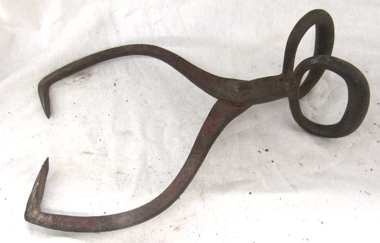 Antique wrought iron ice tongs with a curved handle and ring-shaped loop on one end.