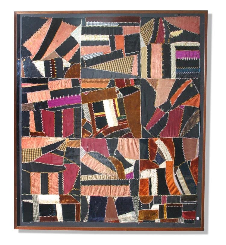 Framed patchwork quilt with geometric blocks and appliqued shapes in reds, pinks, black, and cream.