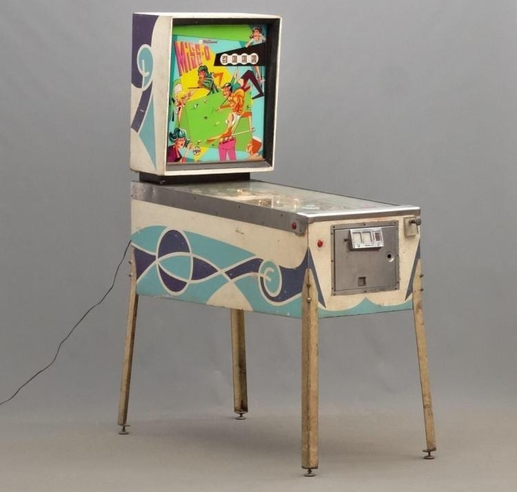 Small vintage pinball machine on four metal legs with colorful panel art and a playfield window.