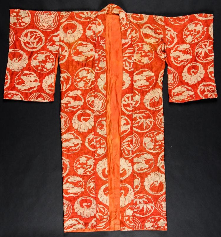 Folded orange Japanese kimono with white circular floral patterns and wide orange collar ribbon on a dark background.