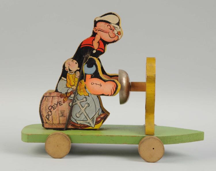 Colorful Popeye the Sailor toy figure standing on a green wooden base with a vertical crank and wheels.
