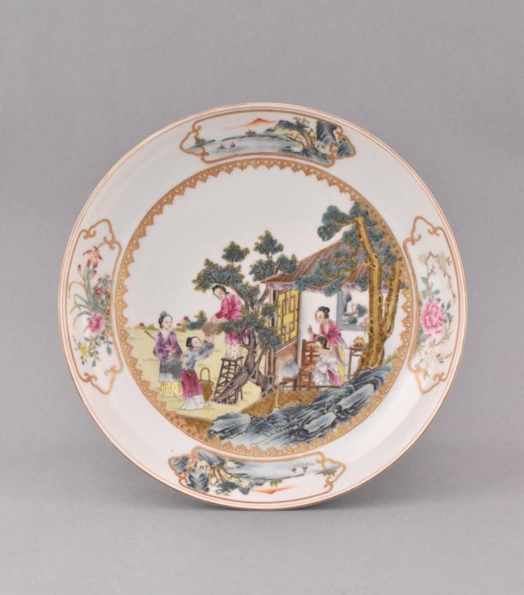 Decorative porcelain plate with colorful figures in a garden scene, surrounded by ornate floral and scroll borders.