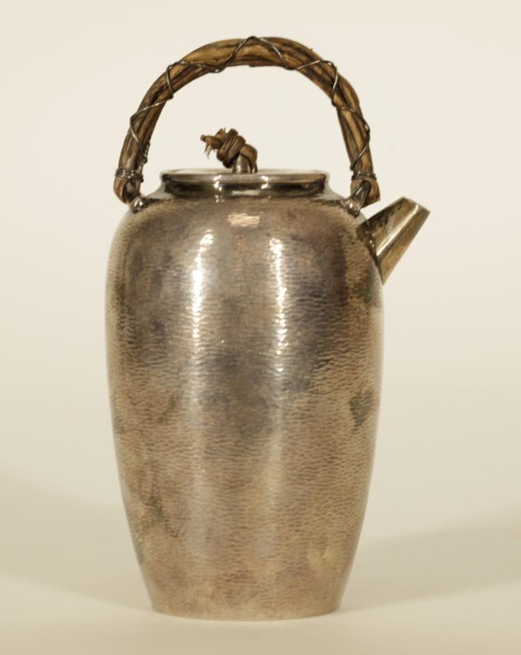 Silver teapot with a hammered texture, arched handle with decorative finials, and a spout visible on a light background.