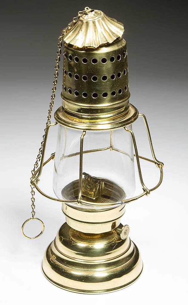 Brass hurricane lantern with perforated sides, ribbed base, glass chimney, and hanging chain with ring.