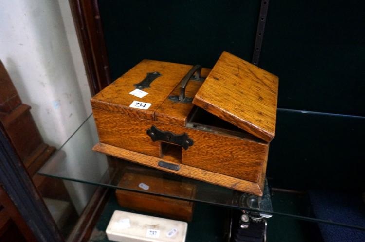 Antique wooden cigar box with hinged lid open, showing brass handle hardware and a divided interior, on a glass display table.